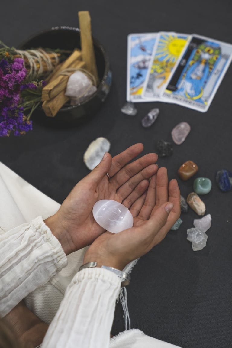 Close-up of hands holding healing stone with tarot cards on surface, promoting spiritual healing.