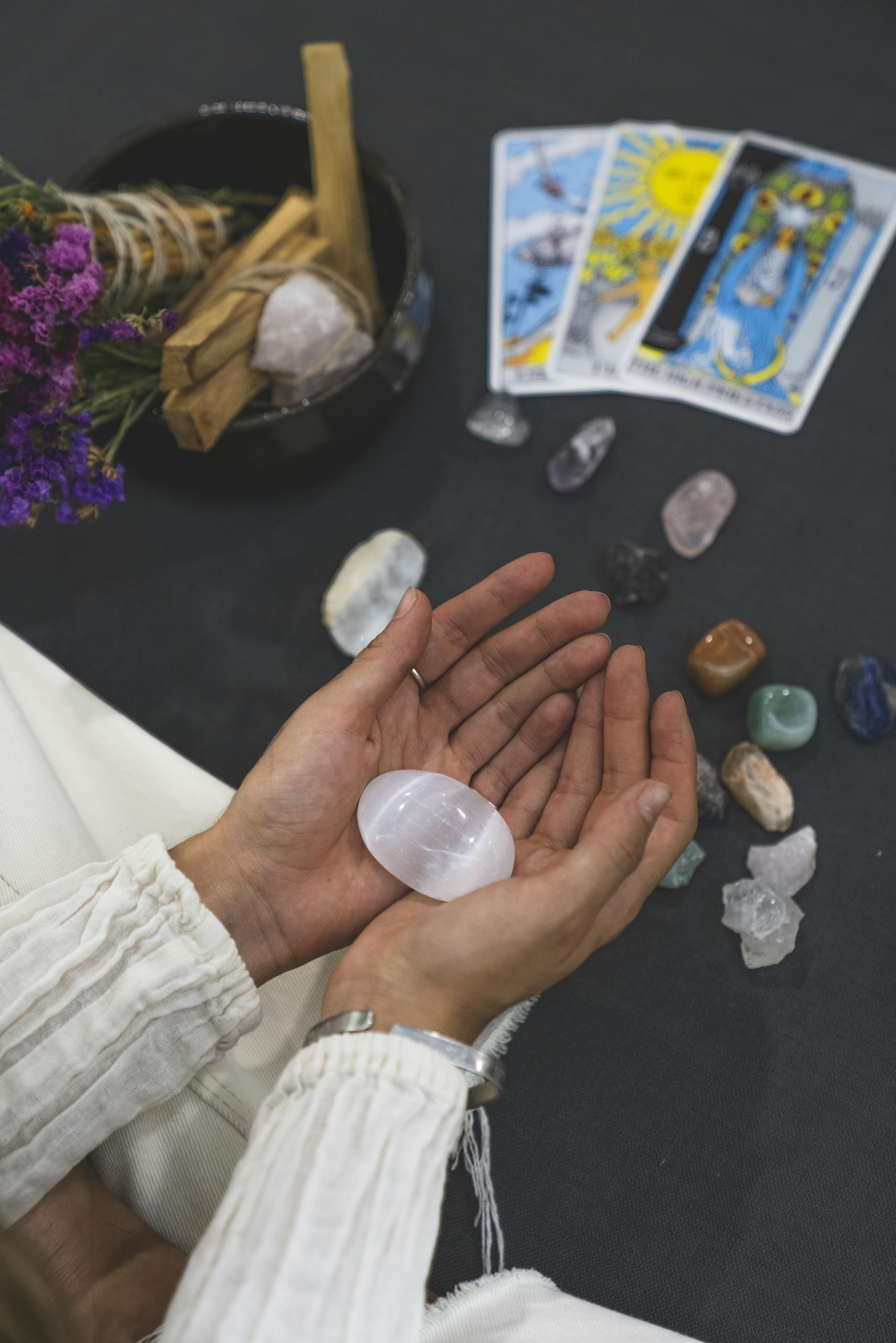 Close-up of hands holding healing stone with tarot cards on surface, promoting spiritual healing.